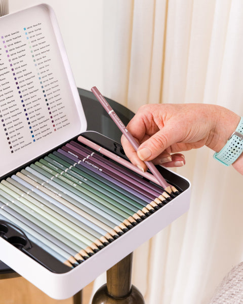 An artist holding a rose-coloured pencil from the Castle Arts Harmonious Colored Pencil Set.” class=